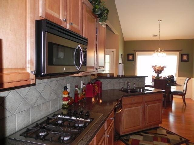 kitchen featuring stainless steel microwave, gas stovetop, a sink, brown cabinetry, and vaulted ceiling