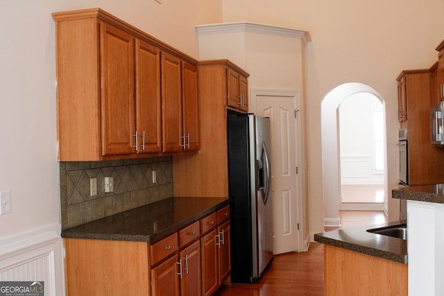 kitchen with stainless steel appliances, decorative backsplash, brown cabinets, arched walkways, and dark wood finished floors