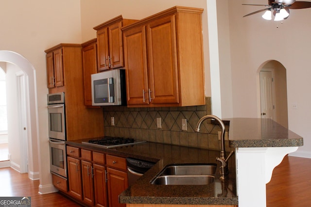 kitchen featuring arched walkways, a sink, appliances with stainless steel finishes, ceiling fan, and a towering ceiling