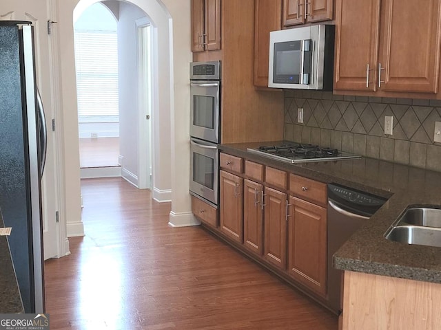 kitchen with stainless steel appliances, dark wood-type flooring, baseboards, tasteful backsplash, and arched walkways