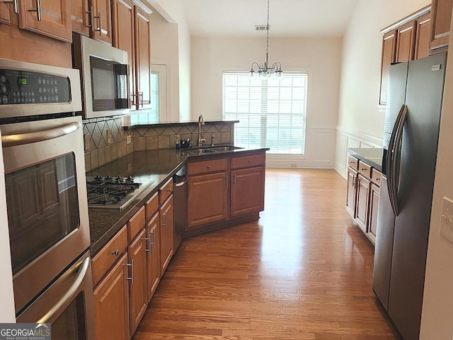 kitchen with stainless steel appliances, a sink, a peninsula, light wood-style flooring, and a chandelier