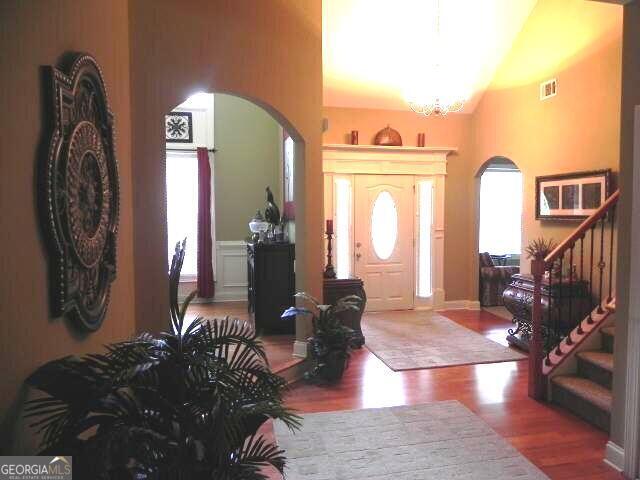 foyer entrance with arched walkways, wood finished floors, stairs, a chandelier, and vaulted ceiling