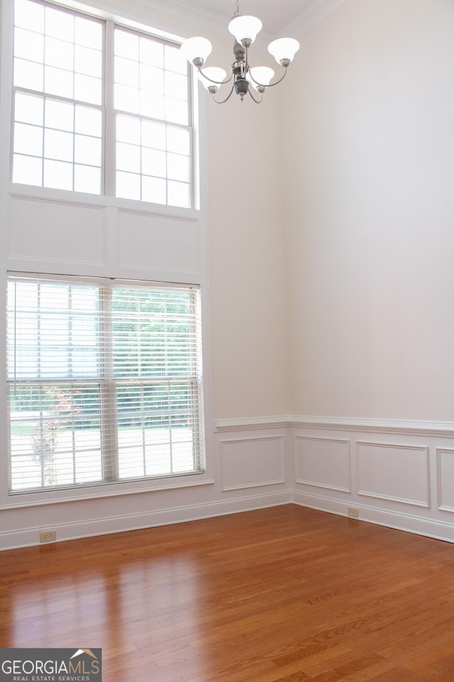 unfurnished dining area with a chandelier, healthy amount of natural light, a wainscoted wall, wood finished floors, and ornamental molding