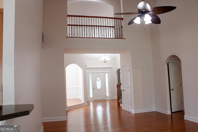 foyer entrance with a high ceiling, wood finished floors, ceiling fan, arched walkways, and a chandelier