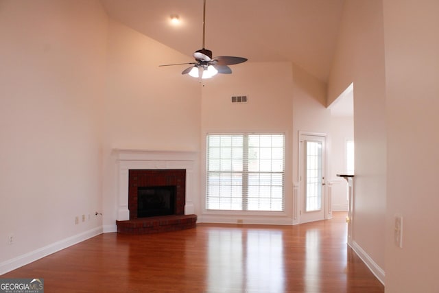 unfurnished living room with wood finished floors, ceiling fan, high vaulted ceiling, baseboards, and a brick fireplace