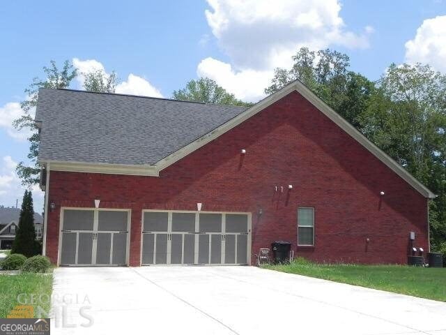 view of side of home with concrete driveway, roof with shingles, a garage, and brick siding