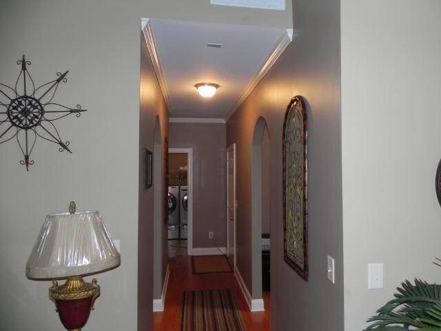 corridor with washer and clothes dryer, crown molding, wood finished floors, arched walkways, and baseboards