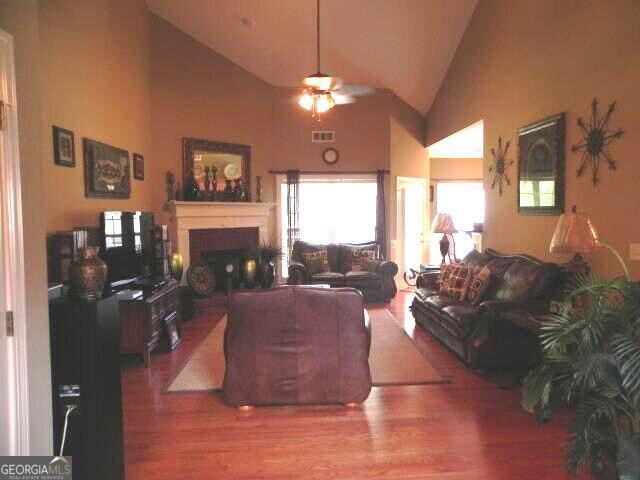 living area with a ceiling fan, a fireplace, wood finished floors, and high vaulted ceiling