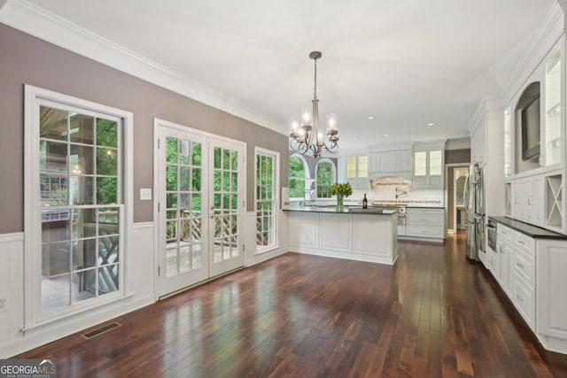 10660 Dunoon Dr, Alpharetta, GA 30022 - kitchen with a peninsula, a chandelier, dark countertops, glass insert cabinets, and dark wood finished floors