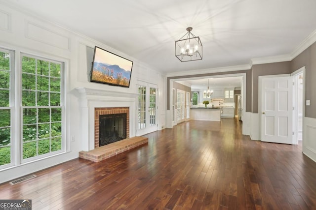 10660 Dunoon Dr, Alpharetta, GA 30022 - unfurnished living room with a chandelier, a decorative wall, dark wood finished floors, ornamental molding, and a brick fireplace