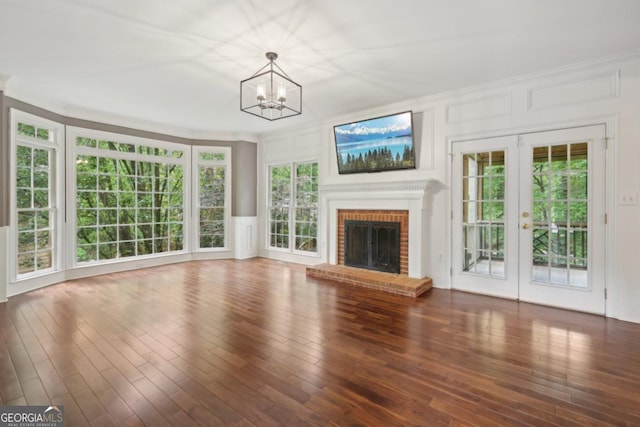 10660 Dunoon Dr, Alpharetta, GA 30022 - unfurnished living room featuring a decorative wall, a chandelier, wood finished floors, french doors, and a brick fireplace