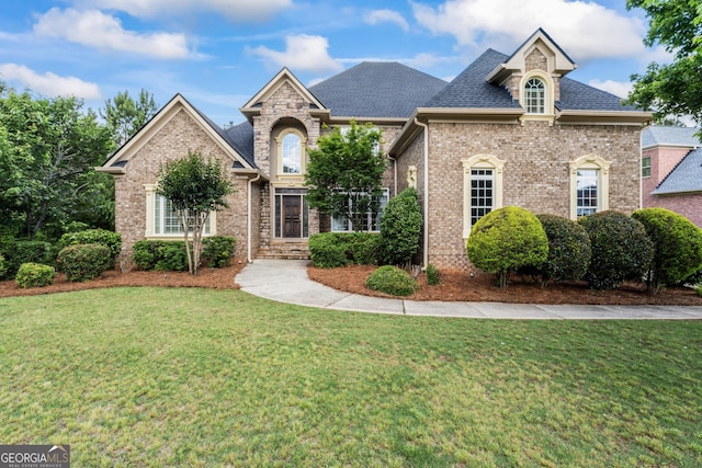 view of front of house with a front lawn, roof with shingles, and brick siding