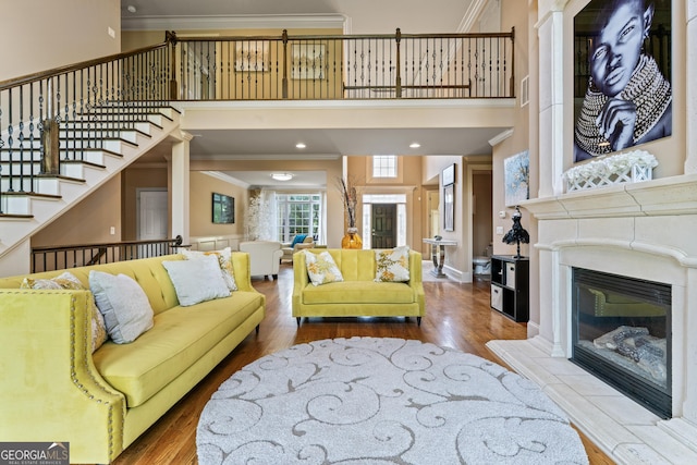living room featuring crown molding, wood finished floors, stairway, a fireplace, and a high ceiling