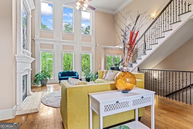 living room featuring a towering ceiling, wood finished floors, ornamental molding, ceiling fan, and a glass covered fireplace