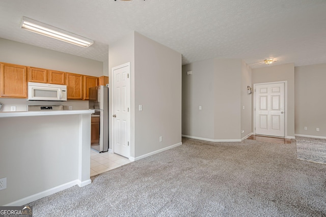 kitchen featuring white microwave, light carpet, freestanding refrigerator, light countertops, and baseboards