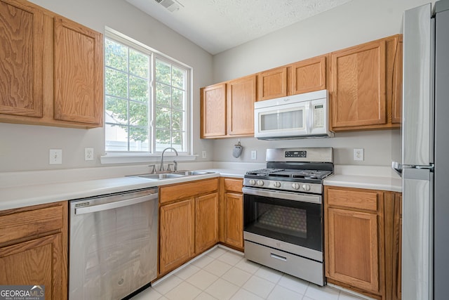 kitchen with appliances with stainless steel finishes, a sink, light countertops, light tile patterned flooring, and a textured ceiling