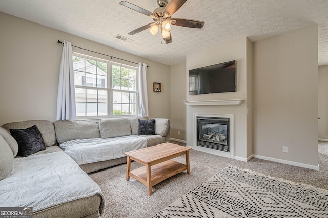 carpeted living room featuring ceiling fan, a glass covered fireplace, a textured ceiling, and baseboards