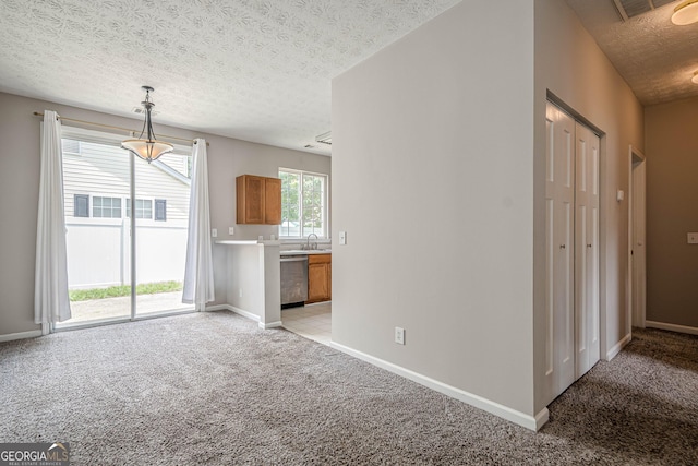 unfurnished living room with light colored carpet, a textured ceiling, baseboards, and a sink
