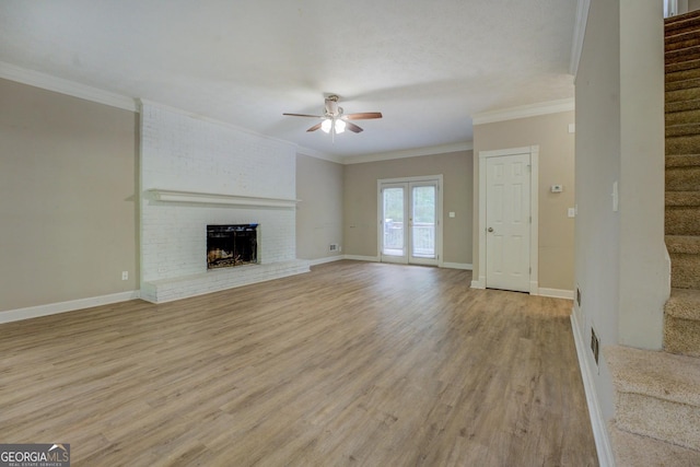 unfurnished living room with ceiling fan, stairs, a fireplace, light wood-style floors, and crown molding