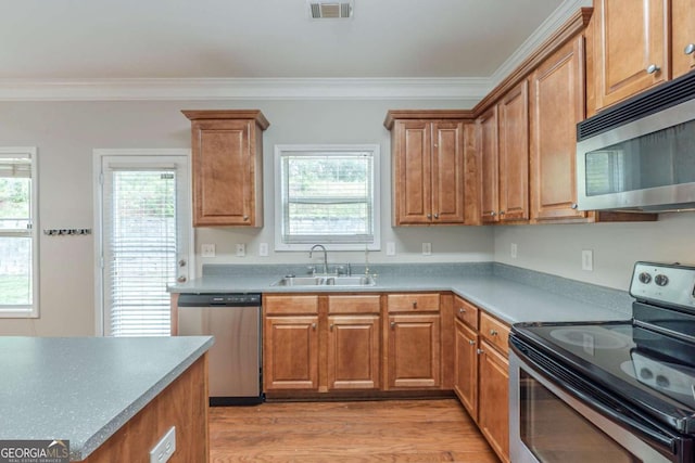 kitchen featuring appliances with stainless steel finishes, a sink, brown cabinets, crown molding, and plenty of natural light