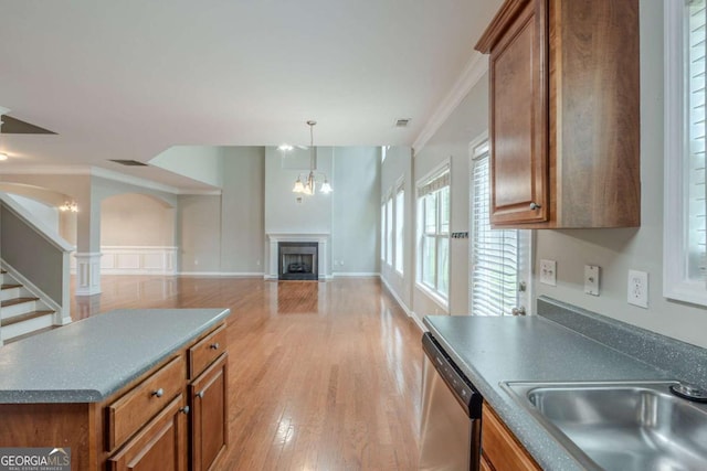 kitchen with a sink, brown cabinetry, crown molding, stainless steel dishwasher, and a fireplace