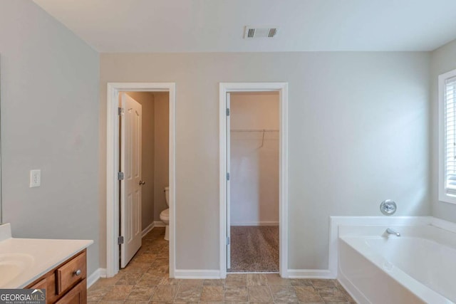 bathroom featuring toilet, vanity, a garden tub, a spacious closet, and baseboards