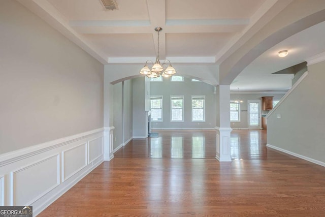 unfurnished dining area featuring a chandelier, arched walkways, coffered ceiling, beam ceiling, and wood finished floors