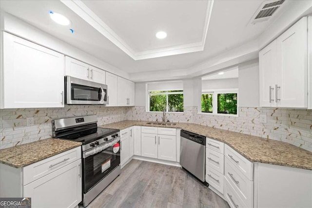 kitchen with appliances with stainless steel finishes, a sink, light wood-type flooring, white cabinets, and recessed lighting