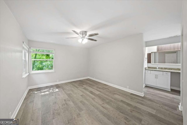 empty room with light wood-type flooring, a ceiling fan, baseboards, and a sink