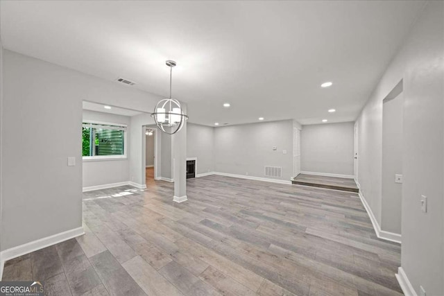 unfurnished living room with wood finished floors, recessed lighting, baseboards, and a chandelier