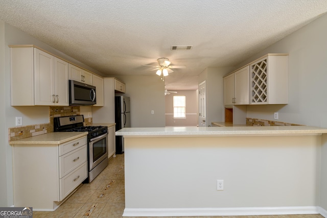 kitchen featuring stainless steel appliances, a peninsula, tasteful backsplash, ceiling fan, and light countertops
