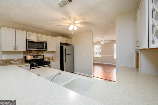 kitchen with stainless steel appliances, ceiling fan, light countertops, decorative backsplash, and a textured ceiling