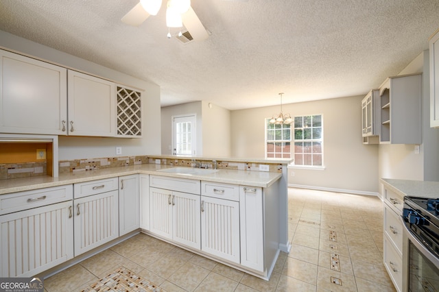 kitchen featuring a peninsula, a sink, stainless steel gas range oven, light countertops, and ceiling fan