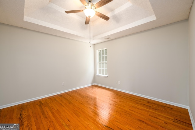 unfurnished room featuring a tray ceiling, baseboards, wood finished floors, ceiling fan, and a textured ceiling