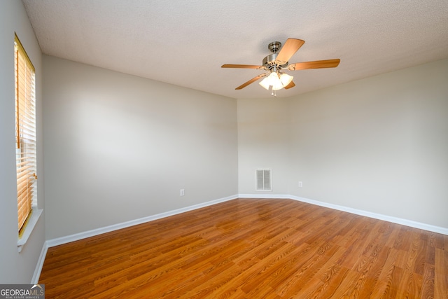 spare room with light wood-type flooring, a ceiling fan, baseboards, and a textured ceiling