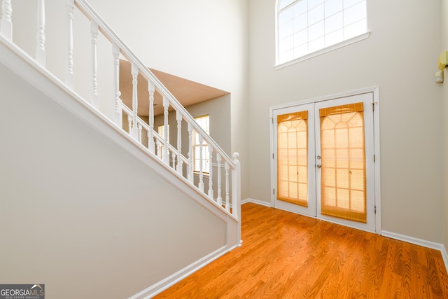foyer entrance featuring a towering ceiling, wood finished floors, stairs, and baseboards