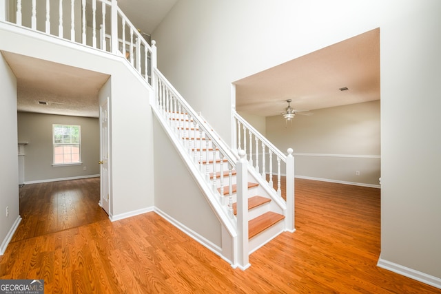stairs featuring wood finished floors, a ceiling fan, and baseboards