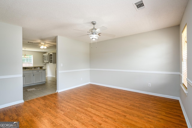 empty room featuring light wood-style floors, ceiling fan, a textured ceiling, and baseboards