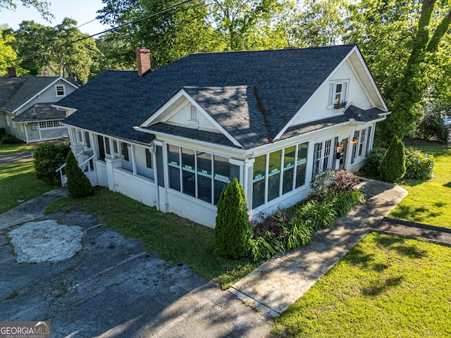 view of front of house featuring a chimney, roof with shingles, a sunroom, and a front lawn