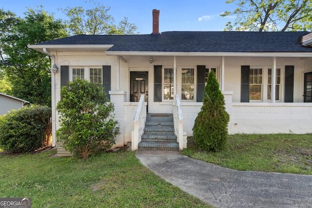 view of front facade featuring a shingled roof, brick siding, a porch, and a front yard