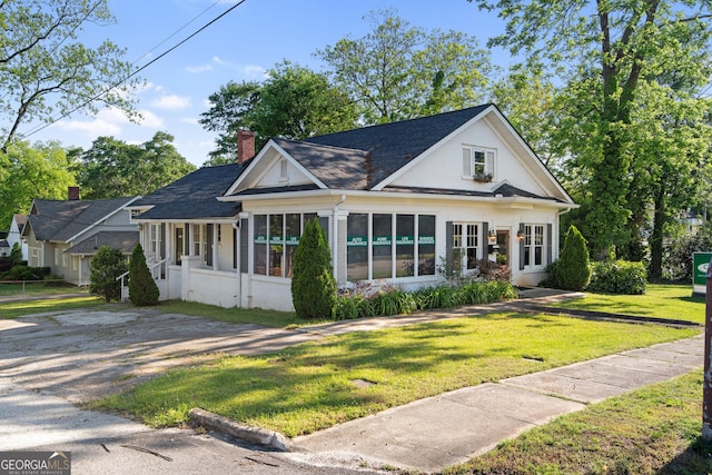 view of front of home with a chimney, a sunroom, a front yard, and roof with shingles