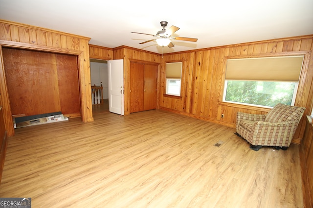 unfurnished room featuring wood walls, light wood-type flooring, a ceiling fan, crown molding, and baseboards