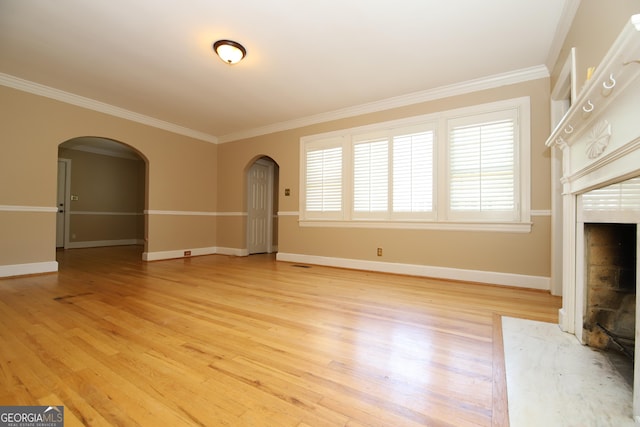 unfurnished living room with arched walkways, crown molding, light wood-type flooring, baseboards, and a fireplace with flush hearth