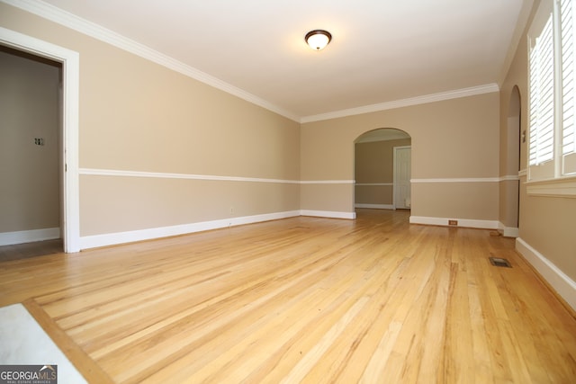 empty room with arched walkways, light wood-style floors, ornamental molding, and baseboards