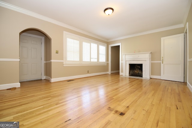 unfurnished living room featuring ornamental molding, light wood-style floors, a fireplace with flush hearth, arched walkways, and baseboards