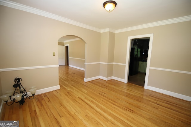 unfurnished room with arched walkways, crown molding, light wood finished floors, and baseboards