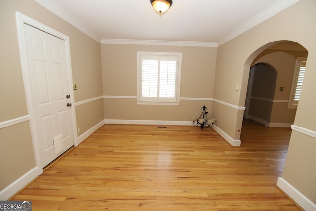 empty room with light wood-style flooring, ornamental molding, arched walkways, and baseboards