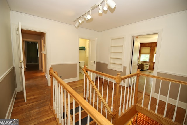 hall featuring an upstairs landing, wood finished floors, built in shelves, rail lighting, and baseboards