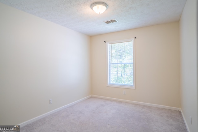 spare room featuring light carpet, baseboards, and a textured ceiling