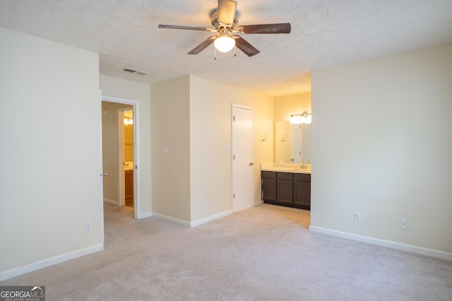 unfurnished bedroom with light colored carpet, a textured ceiling, baseboards, ensuite bathroom, and a ceiling fan